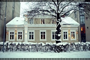 Un edificio de dos pisos con fachada simétrica, ventanas grandes y techo cubierto de nieve.