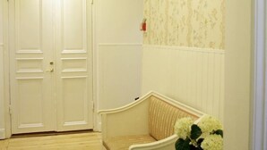 A hallway with a white door, a bench, a white dresser, and a chandelier. - Hotel Kungsängstorg (Uppsala)