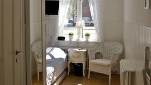 A small, well-lit bedroom with a bed, a chair, a small table, and a window with curtains. - Hotel Kungsängstorg (Uppsala)