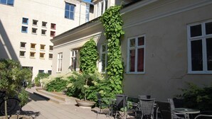 A building with a large ivy-covered wall, outdoor seating area with chairs and tables, and a paved walkway. - Hotel Kungsängstorg (Uppsala)