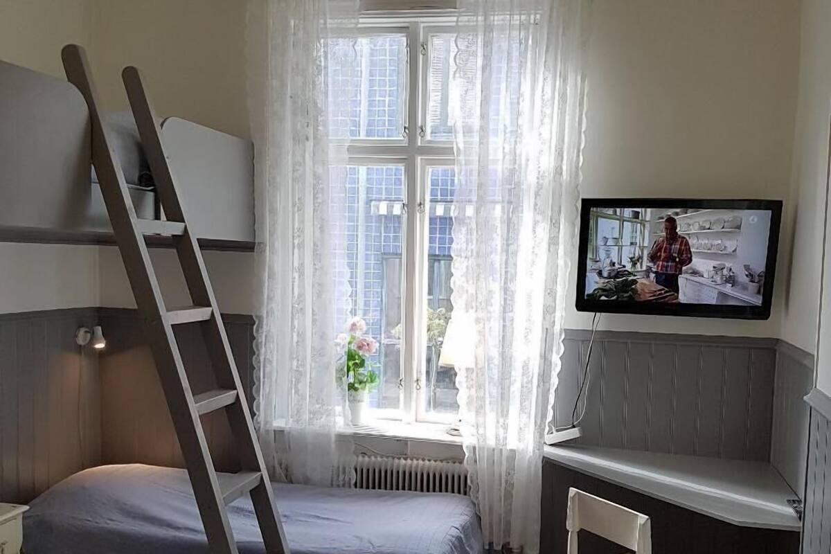 A room with two beds, a TV, a window with curtains, and a wooden floor.