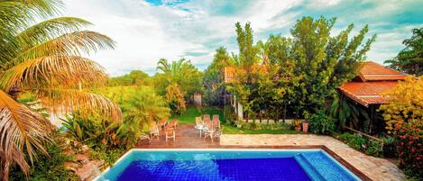 Une piscine entourée d’une végétation luxuriante et une maison avec un toit en tuiles.