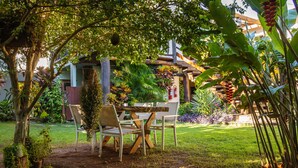 An outdoor seating area with a wooden table and chairs, surrounded by lush greenery and a fire extinguisher. - Pousada Chamamé (Bonito)
