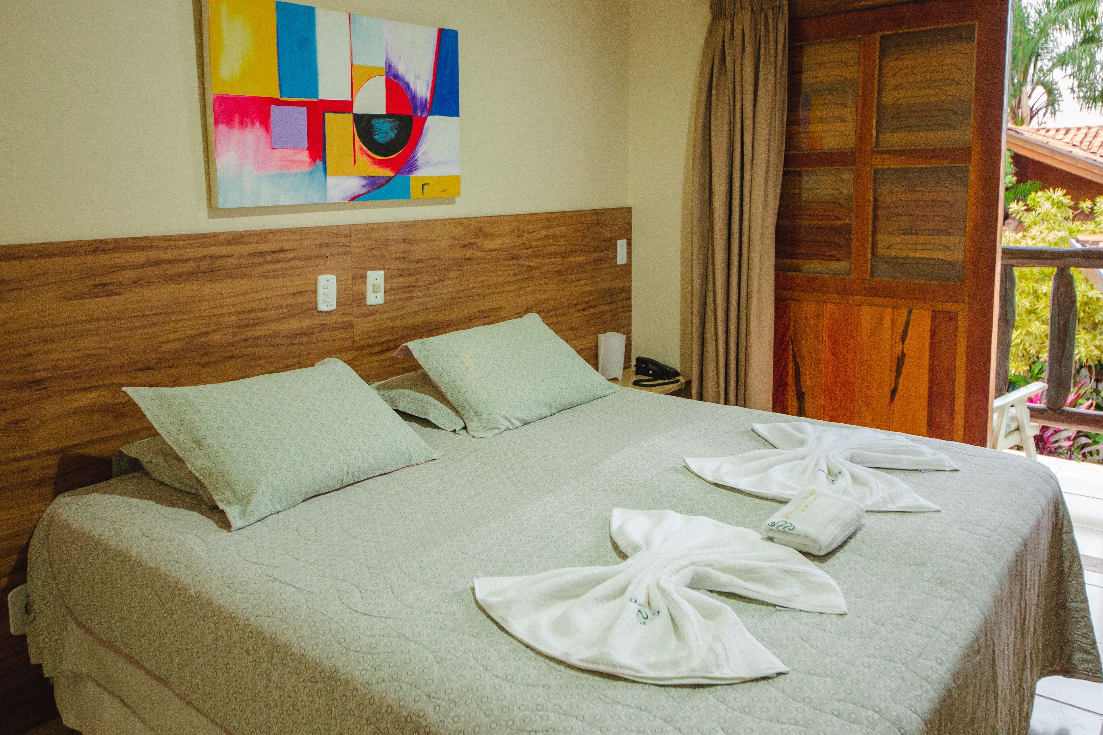 Hotelkamer met een groot bed, een houten hoofdbord, een kleurrijk abstract schilderij en uitzicht op de omgeving.