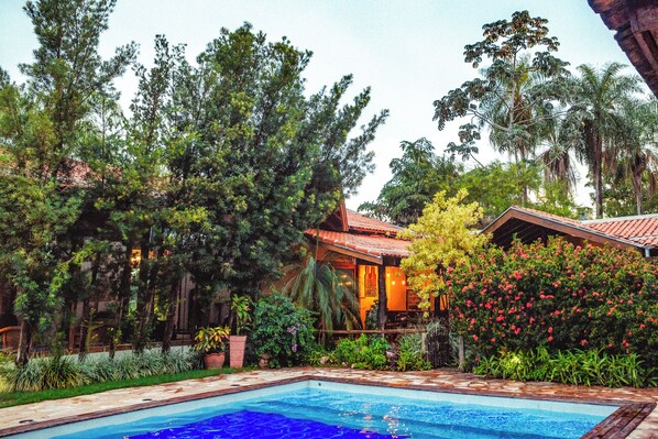 A pool surrounded by lush greenery and a building with a red-tiled roof. - Pousada Chamamé (Bonito)
