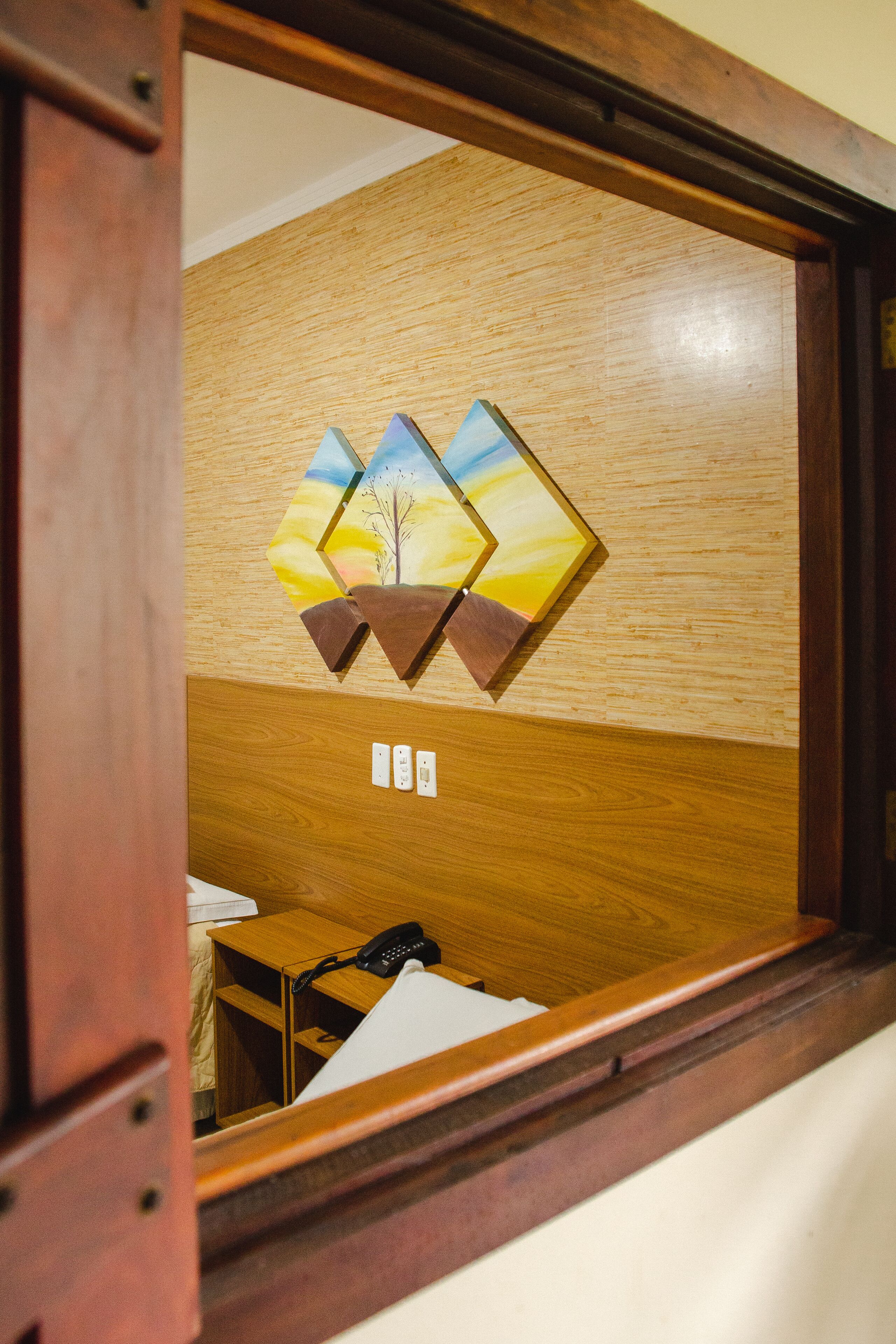 A wooden wall with a geometric artwork and a small wooden table with a telephone.