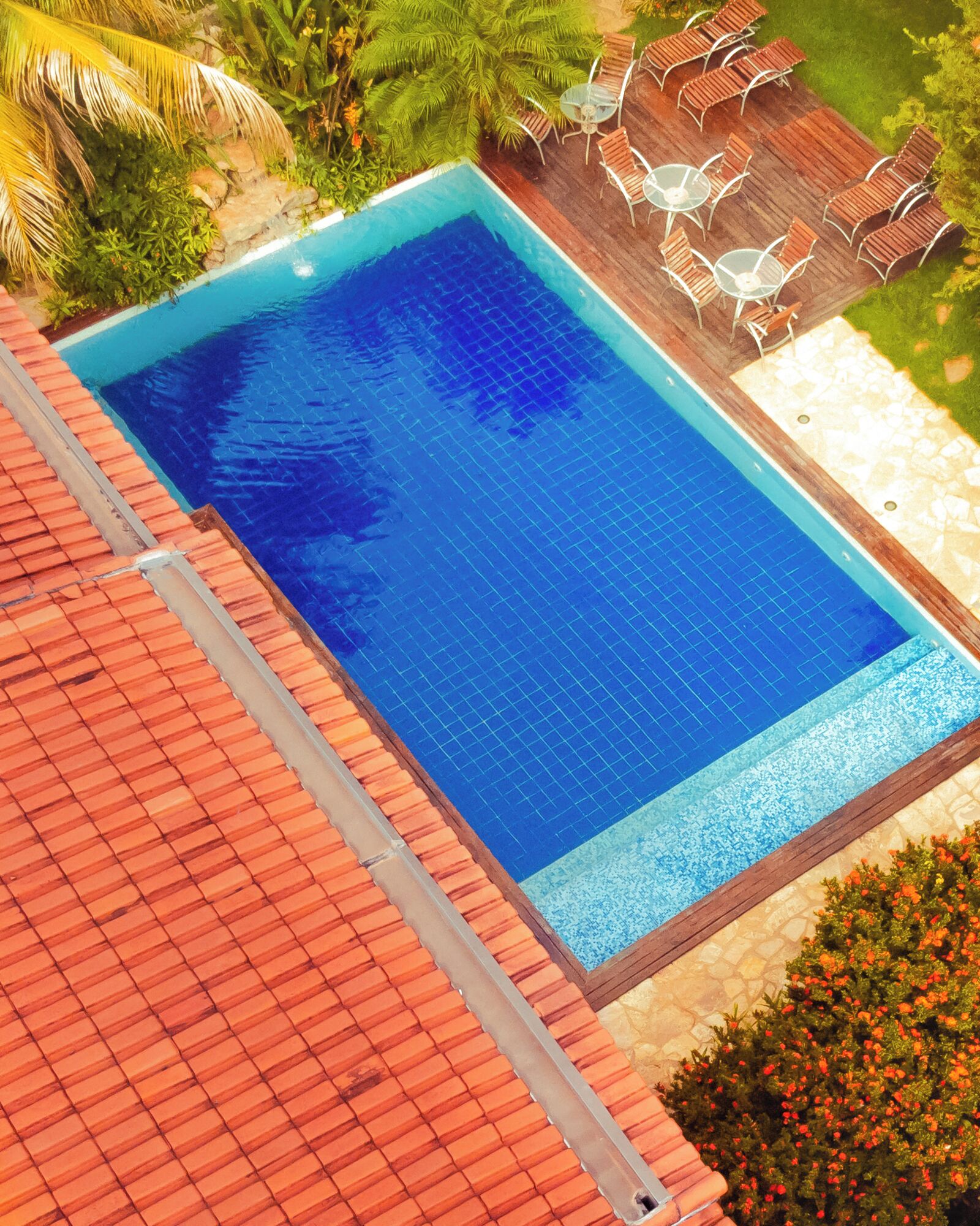 A rectangular swimming pool with a tiled edge, surrounded by a wooden deck and outdoor furniture.