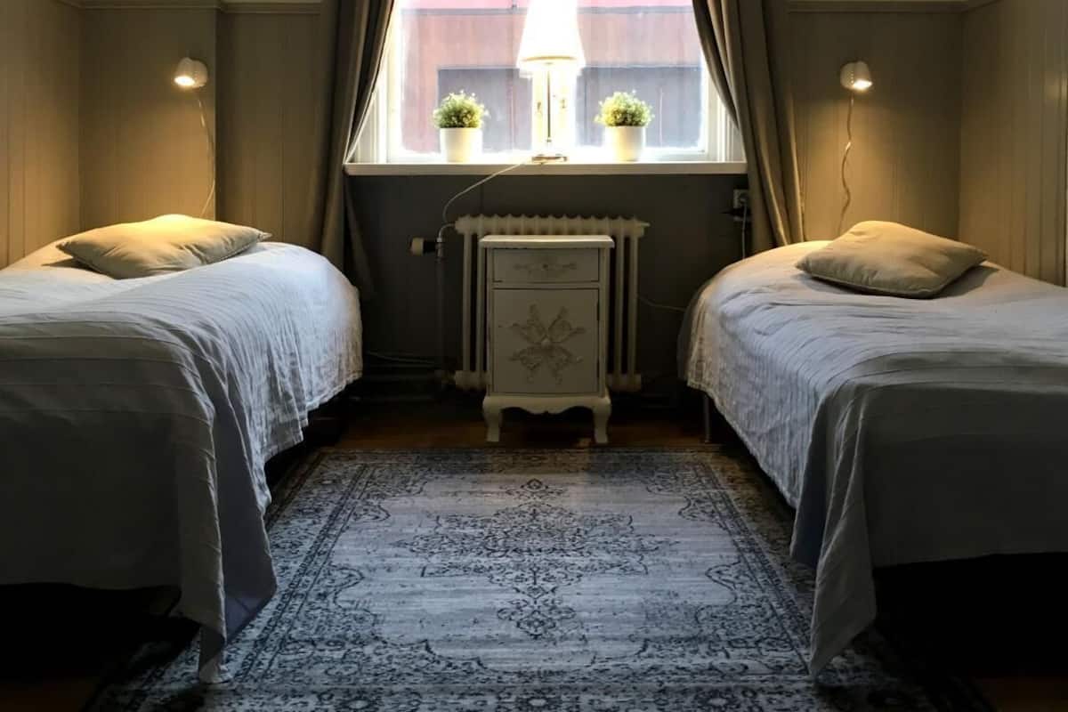 A room with two beds, a radiator, a lamp, and a window with curtains.