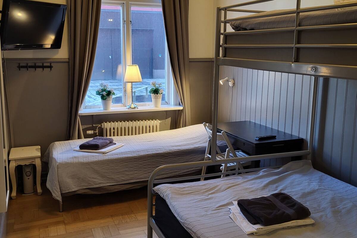 Een slaapzaal met twee eenpersoonsbedden, een stapelbed, een televisie, een radiator en een raam met gordijnen.