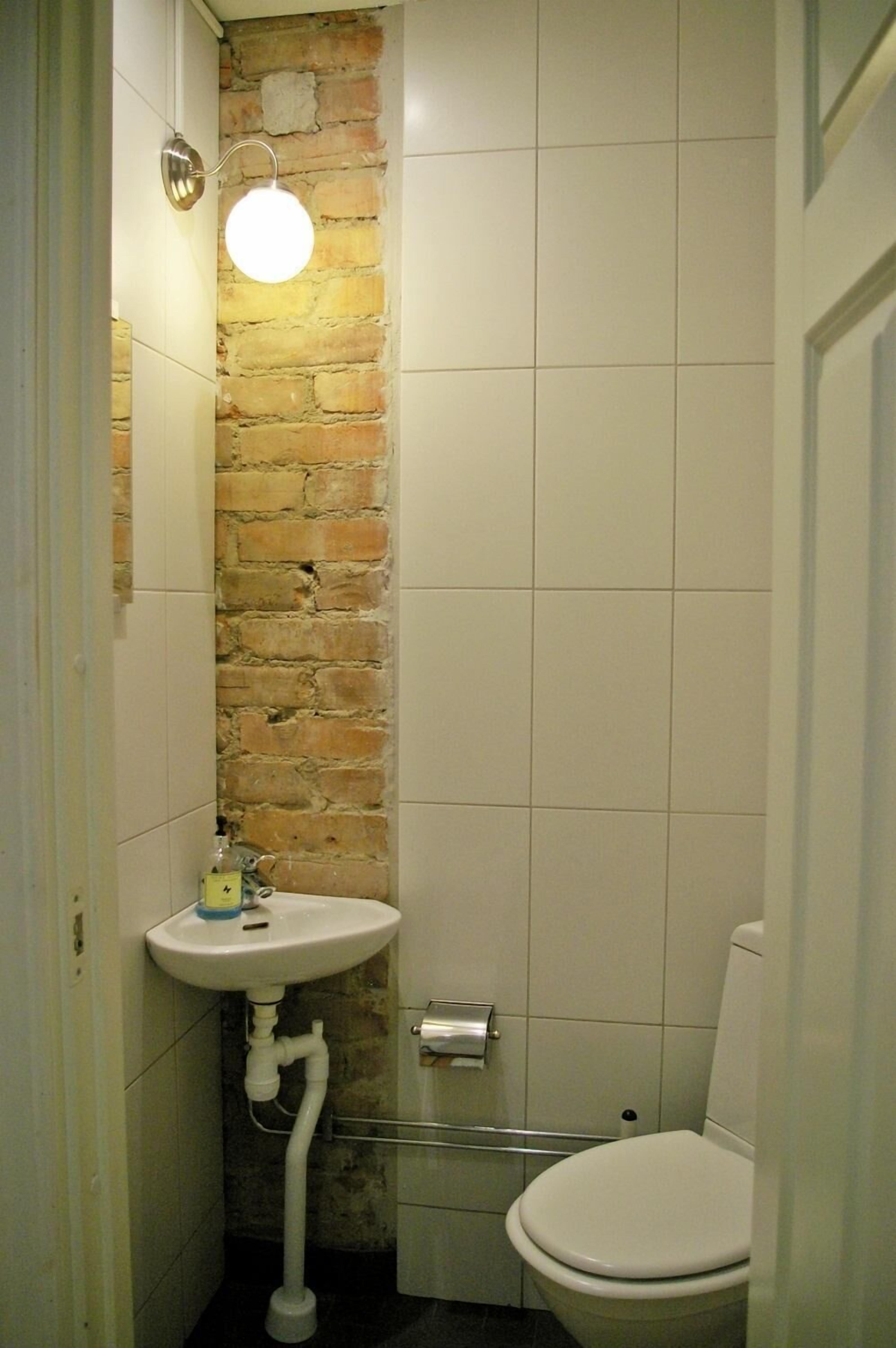 Un baño pequeño con un lavabo blanco, un inodoro y una pared de ladrillo.