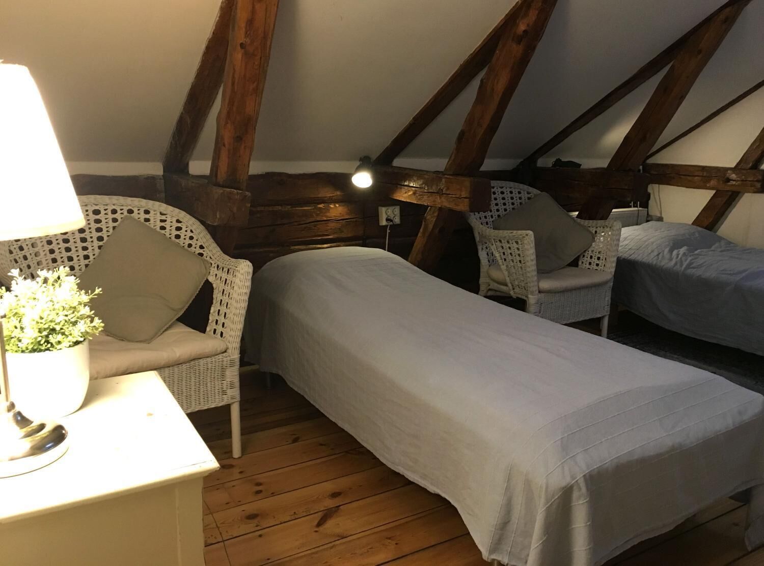 A cozy attic bedroom with two single beds, wicker furniture, and a lamp.
