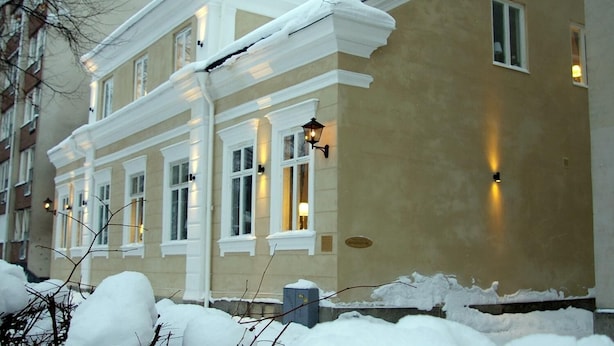 Un edificio de dos pisos con fachada color crema, detalles blancos y numerosas ventanas. Se ve nieve en el techo y en el suelo.