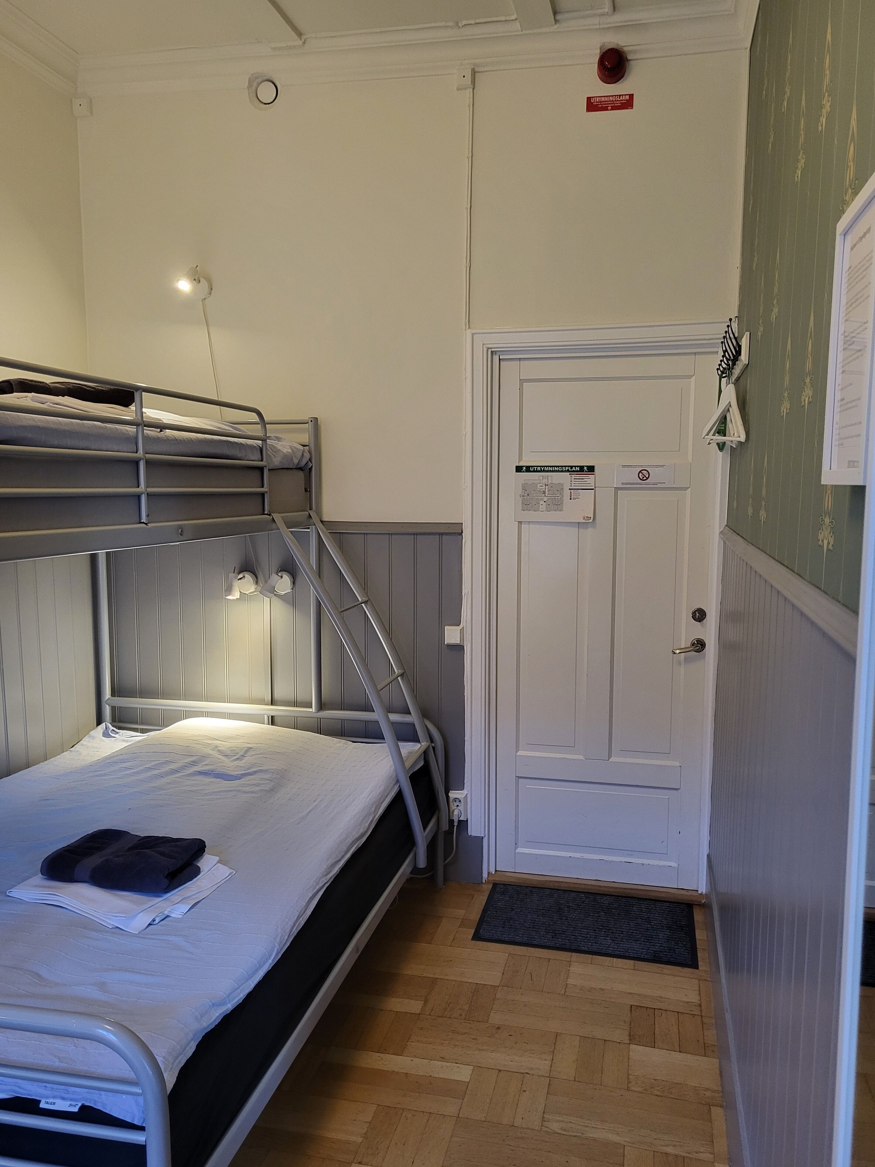 A bunk bed with a ladder, a white door with a sign, and a wooden floor.