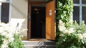 A building entrance with a wooden door, steps, and a potted plant.