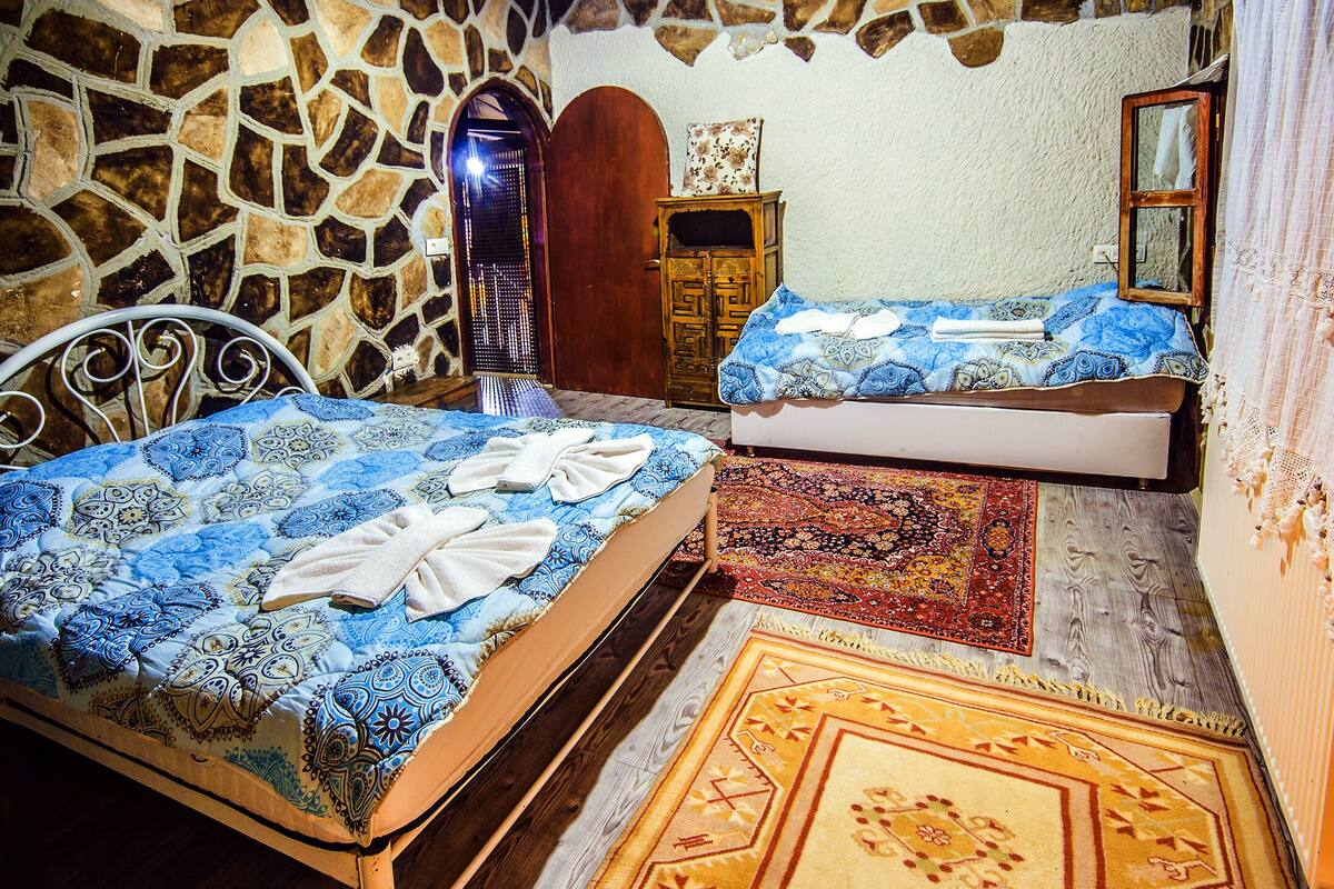 A room with two beds, a stone wall, a wooden wardrobe, and a patterned rug.