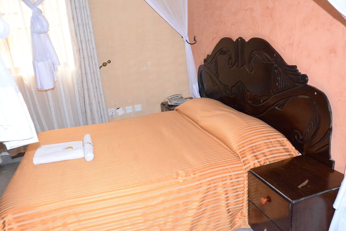 A neatly made bed with a striped orange bedspread, a wooden headboard, and a small bedside table with a drawer.