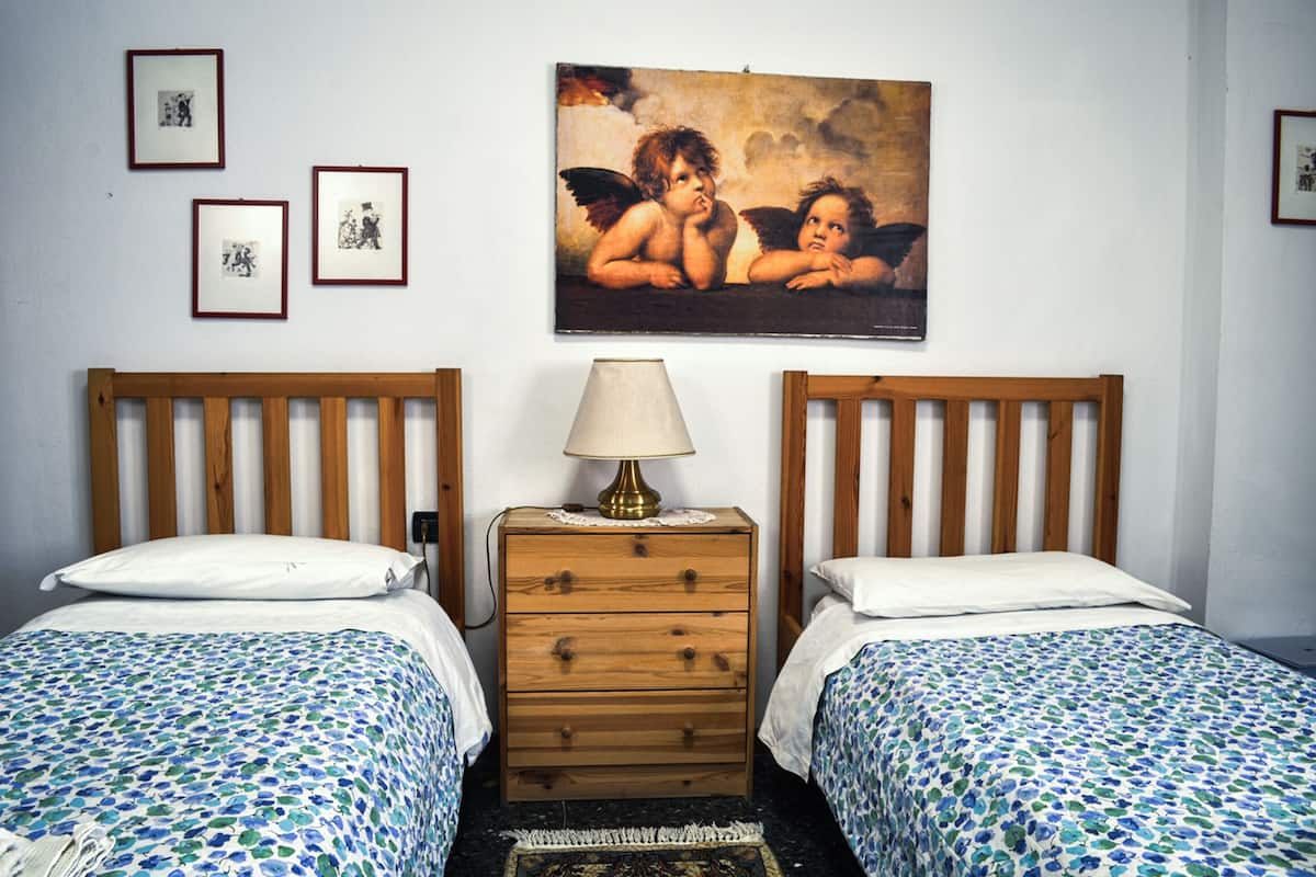 Une chambre avec deux lits, une commode en bois, une lampe et un tableau au mur.