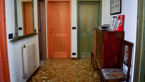 A hallway with a tiled floor, wooden doors, a radiator, and a chair with a patterned cushion. - Bed&Breakfast Arcobaleno (Bologna)