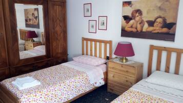 Un dormitorio con dos camas individuales, un armario de madera, una mesita de noche con lámpara y cuadros enmarcados en la pared.