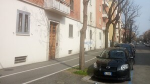 A row of multi-story residential buildings with balconies, a black car parked on the street, and a clear sky. - Bed&Breakfast Arcobaleno (Bologna)