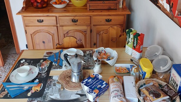 A wooden kitchen with a coffee table, a cabinet with food items, and a painting on the wall. - Bed&Breakfast Arcobaleno (Bologna)