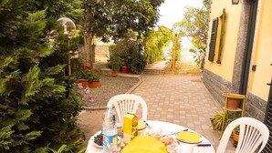 An outdoor dining area with a table set for two, surrounded by potted plants and a brick pathway. - B&B Pervinca (Rocca Grimalda)