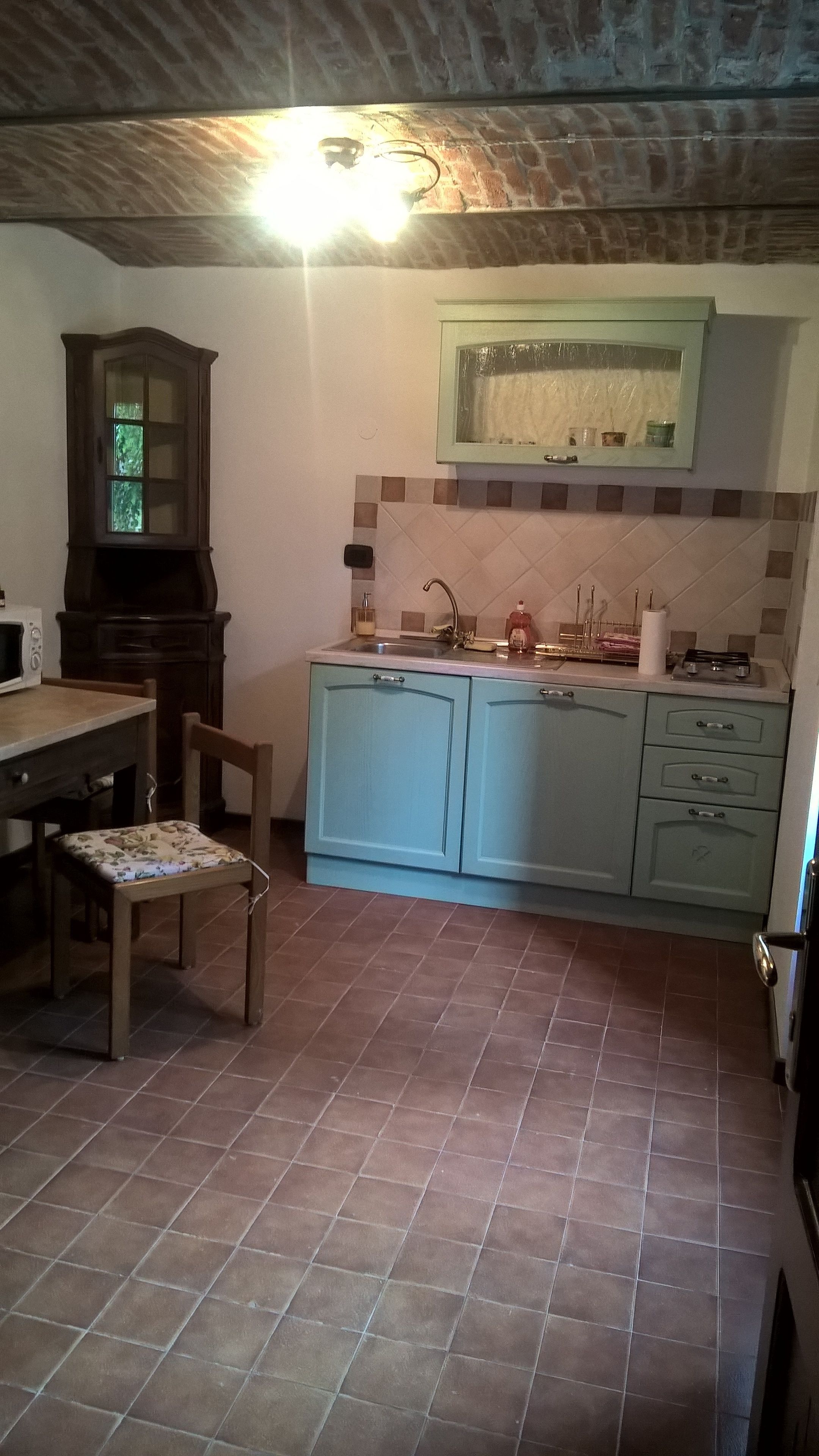 Eine Küche mit Fliesenboden, einem Holzespeisetisch mit Stühlen, einem Schrank und einer Mikrowelle.