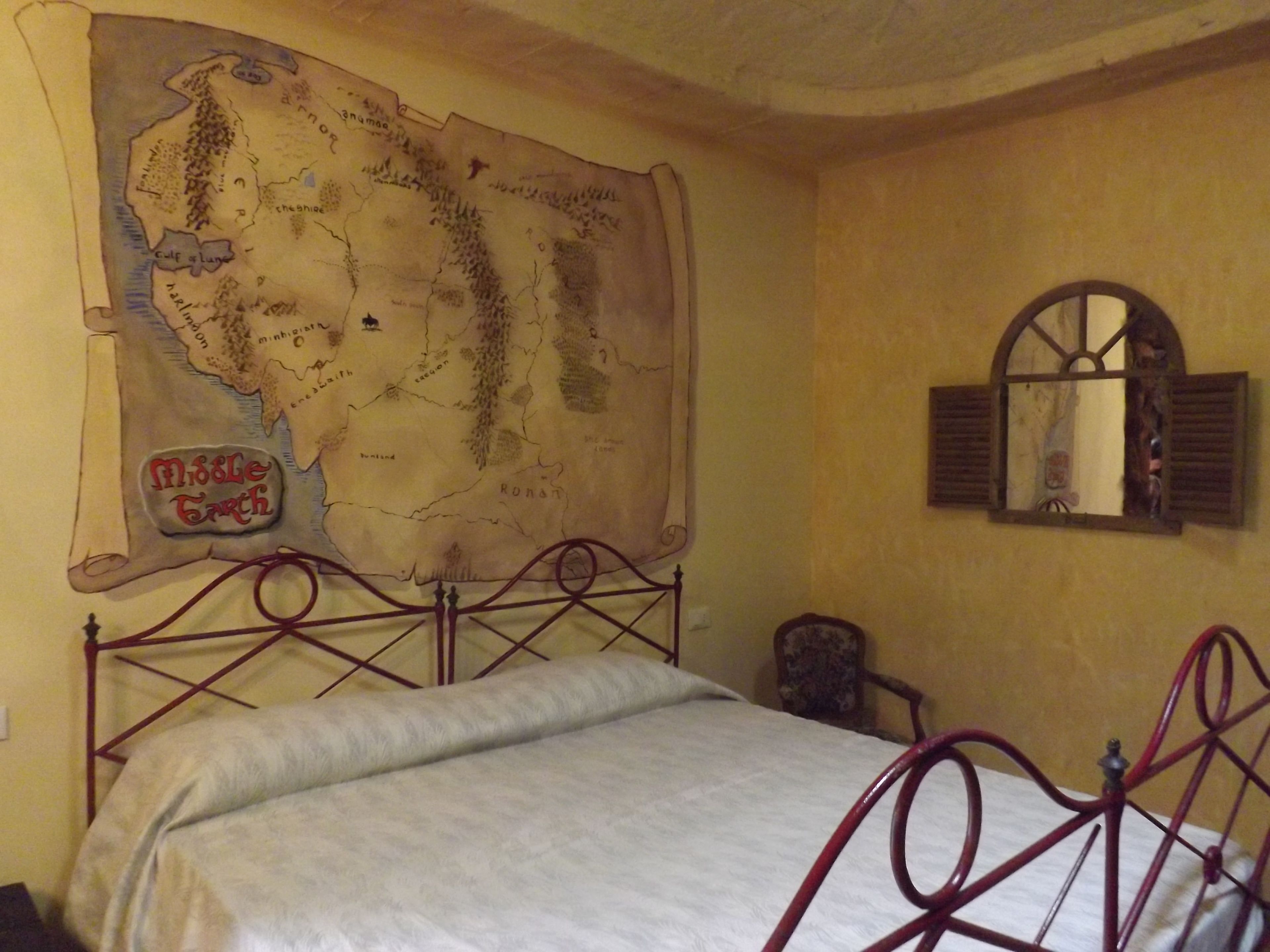 A bedroom with a large map on the wall, a bed with a metal frame, and a wooden chair.