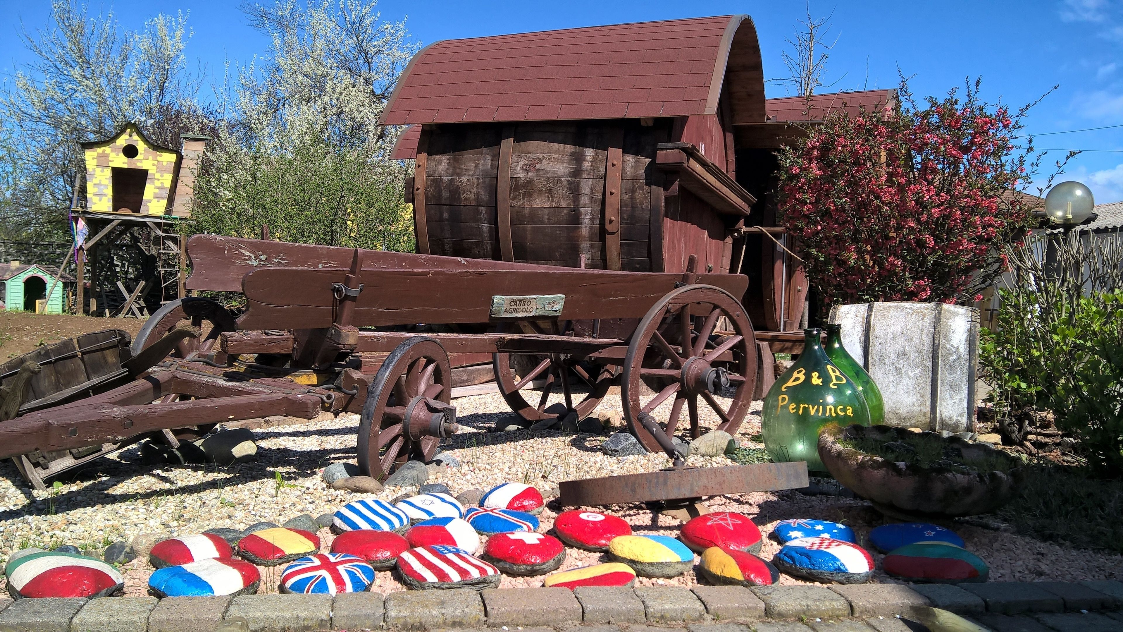 A rustic wooden structure with a red roof, a wheelbarrow, and colorful painted stones.