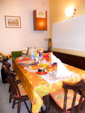 A dining area with a table set for a meal, chairs, a framed picture on the wall, and a radiator. - B&B Pervinca (Rocca Grimalda)