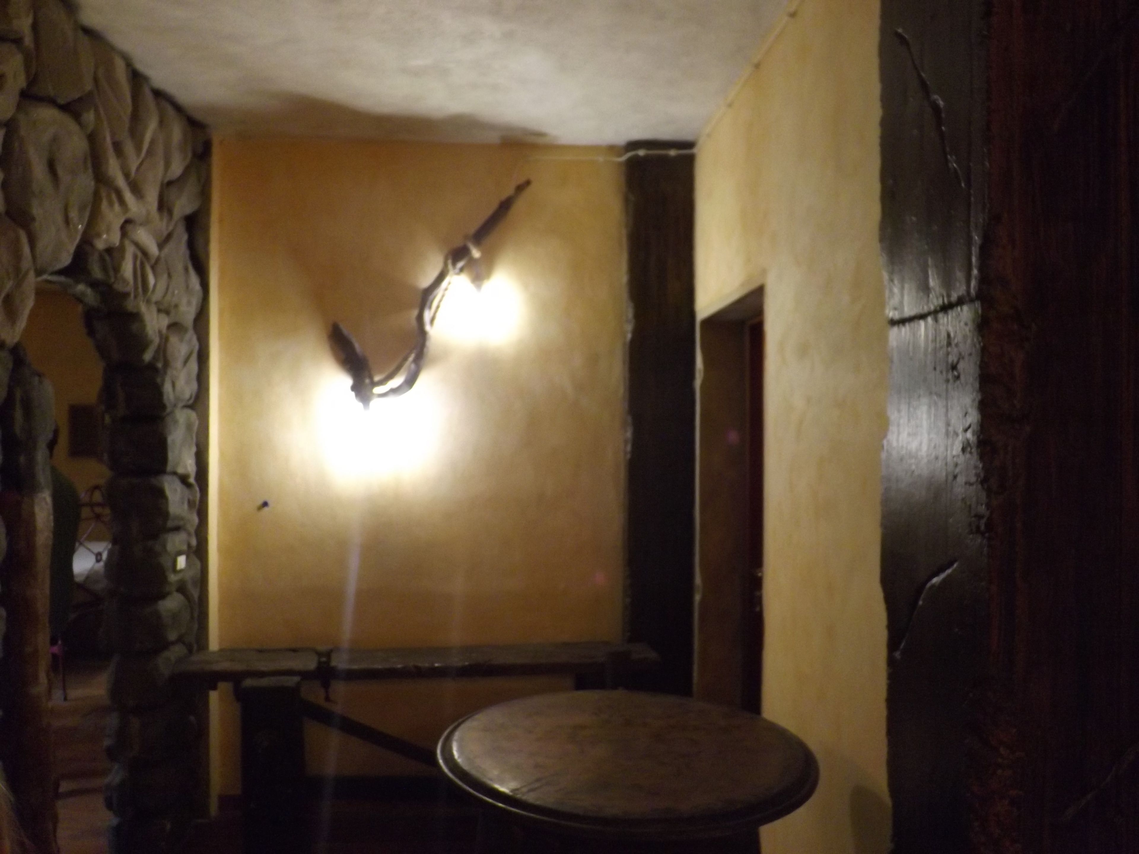Una habitación con pared de piedra, una mesa redonda y una lámpara.