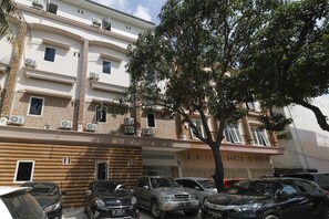 A multi-story building with air conditioning units, a parking area with several cars, and a tree in front. - RedDoorz Plus near RS Royal Prima (Medan)