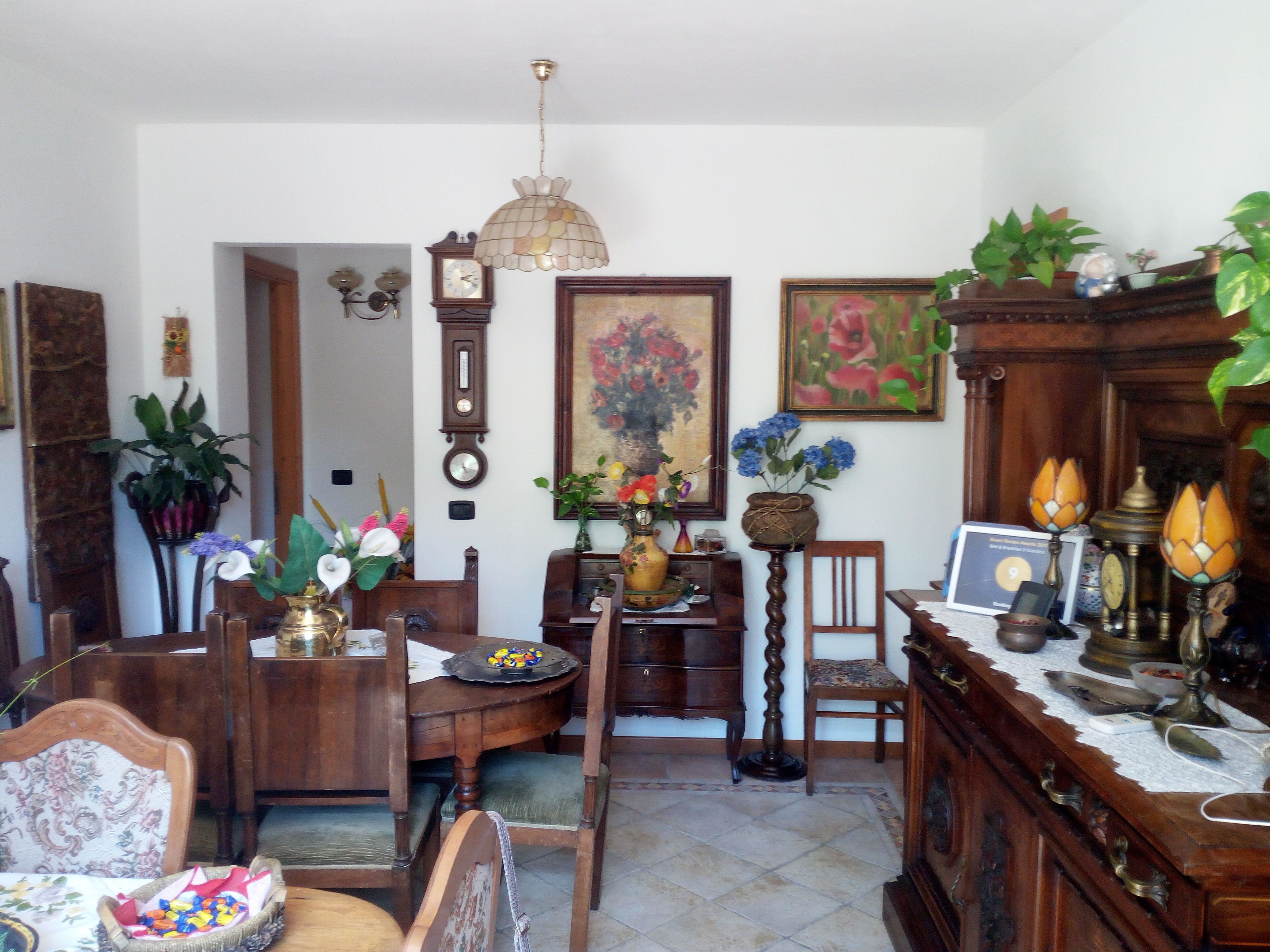 A traditional dining room with wooden furniture, a chandelier, and various decorative items including a clock and paintings.