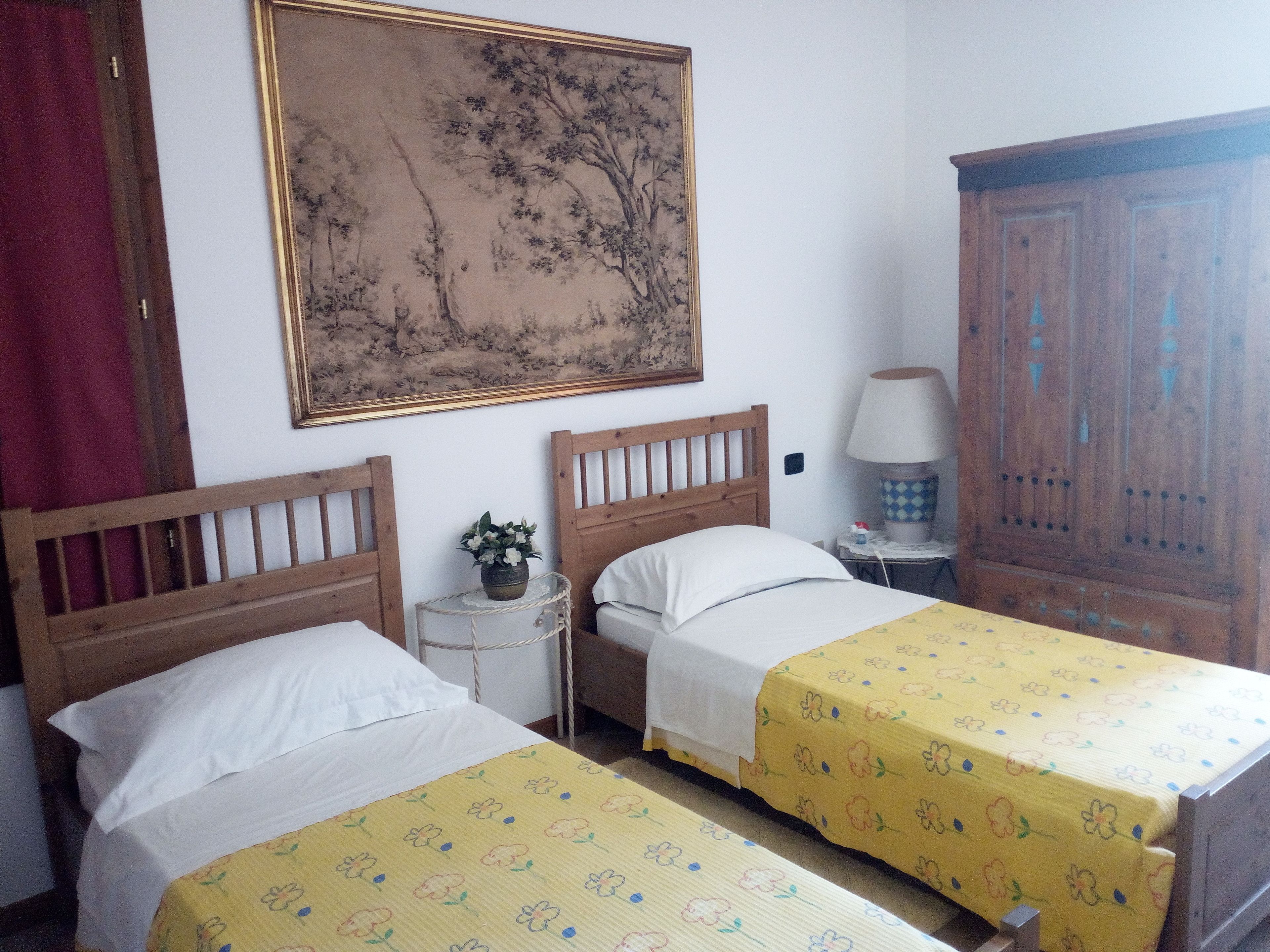 A room with two wooden beds, a nightstand with a lamp, a wooden wardrobe, and a large framed painting on the wall.