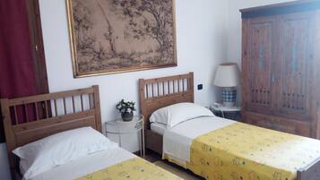 A room with two wooden beds, a nightstand with a lamp, a wooden wardrobe, and a large framed painting on the wall.