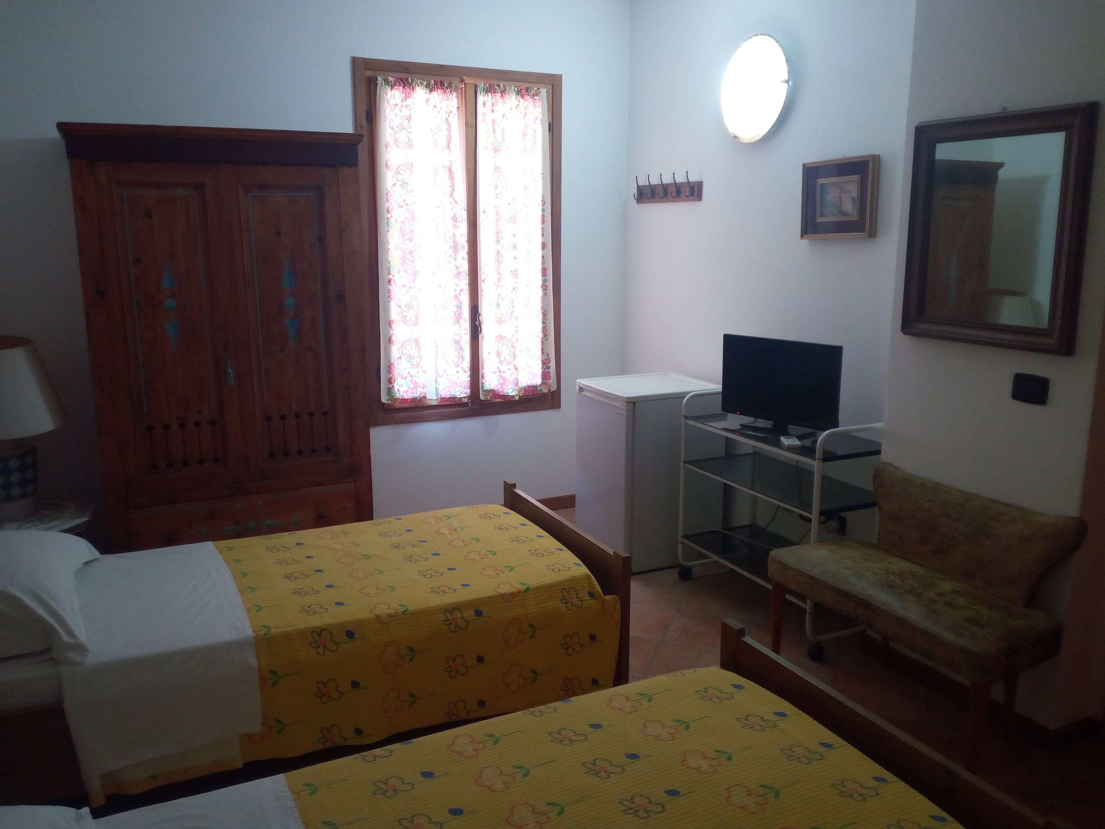 Quarto com duas camas, uma escrivaninha, uma cadeira, uma televisão e um guarda-roupa.