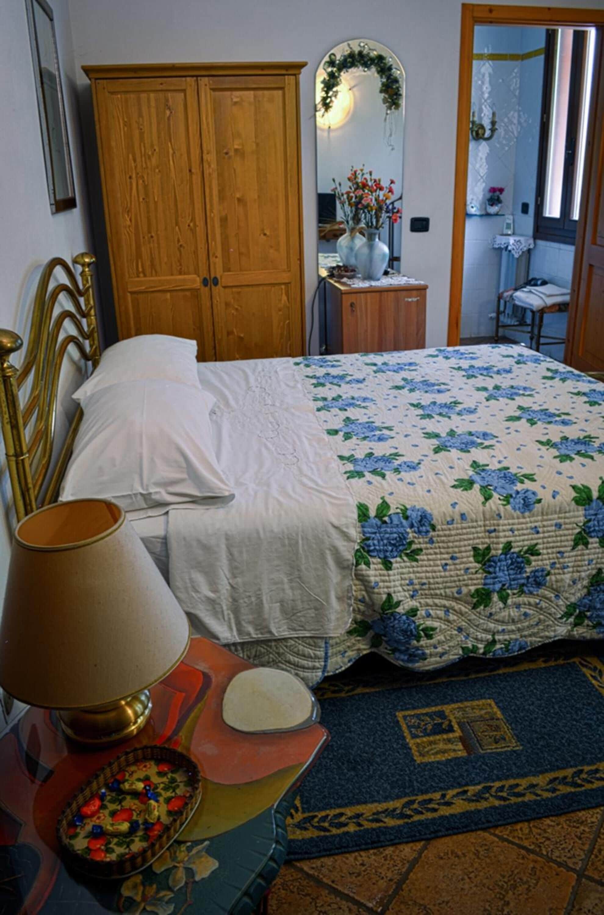 Un dormitorio con cama, armario de madera, espejo, lámpara y una mesita con bandeja.
