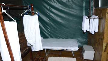 Una habitación pequeña y cerrada con una cama, un banco y un tendedero.