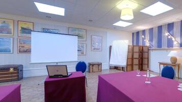 Une salle de conférence équipée d’un tableau blanc, d’un ordinateur portable posé sur une table et d’un écran de projection.