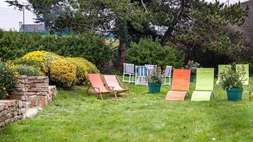 Un espacio al aire libre con césped, un muro de piedra, un árbol y varios sillones y macetas.