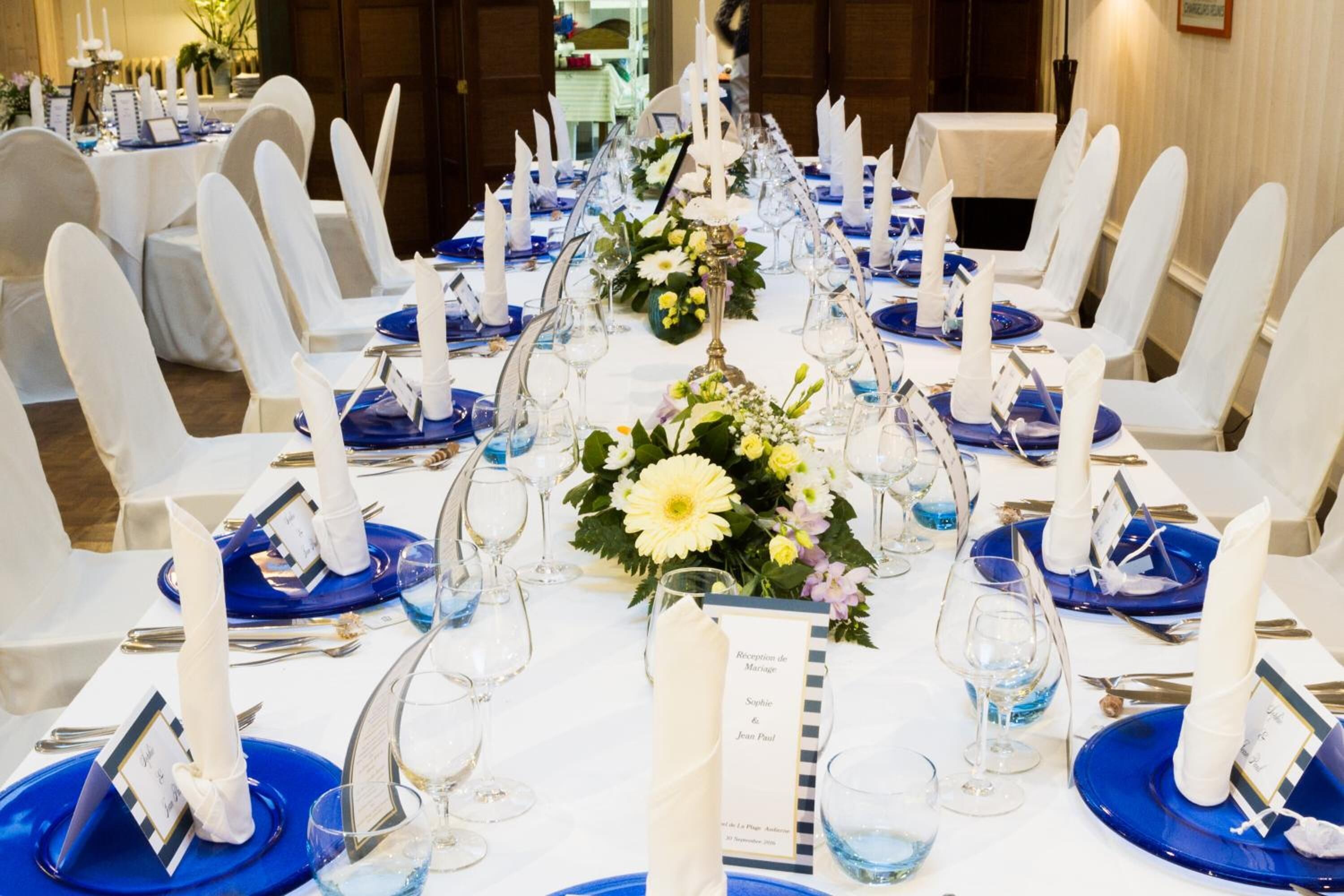A banquet hall with round tables set for a formal event, featuring blue tablecloths, white chairs, and floral centerpieces.