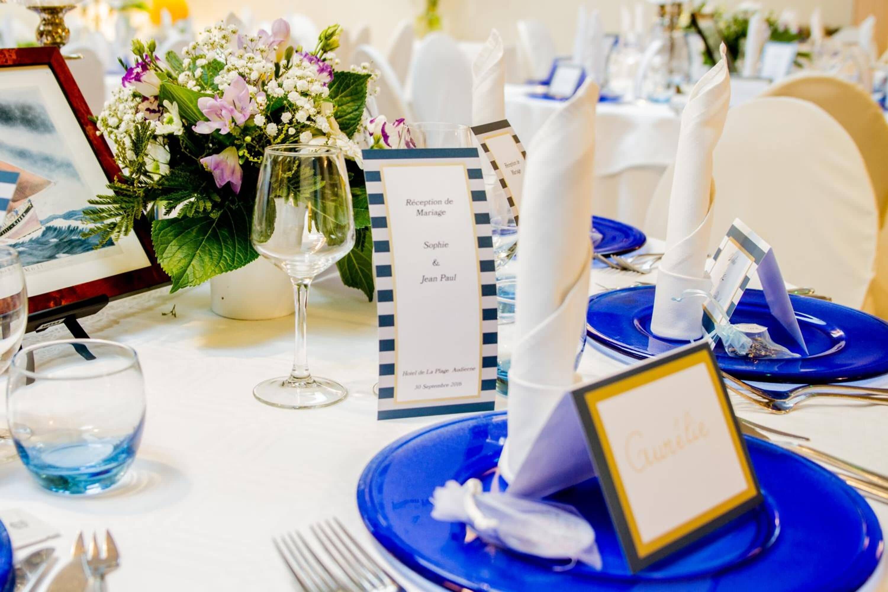 A reception area with a reception desk, a framed picture, a vase with flowers, and a table set with blue plates and white napkins.