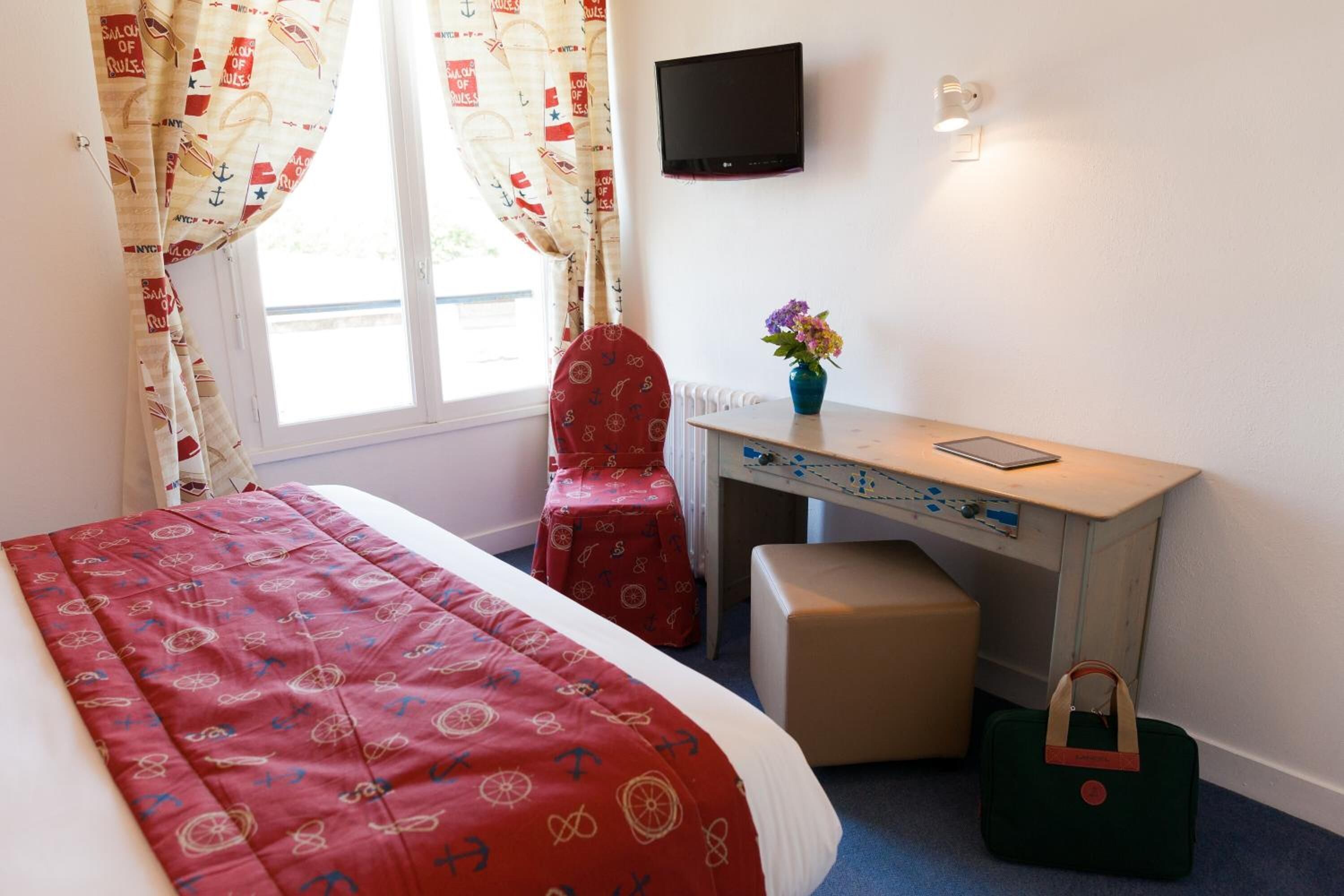 A hotel room with a bed, a desk, a chair, a TV, and a window with curtains.