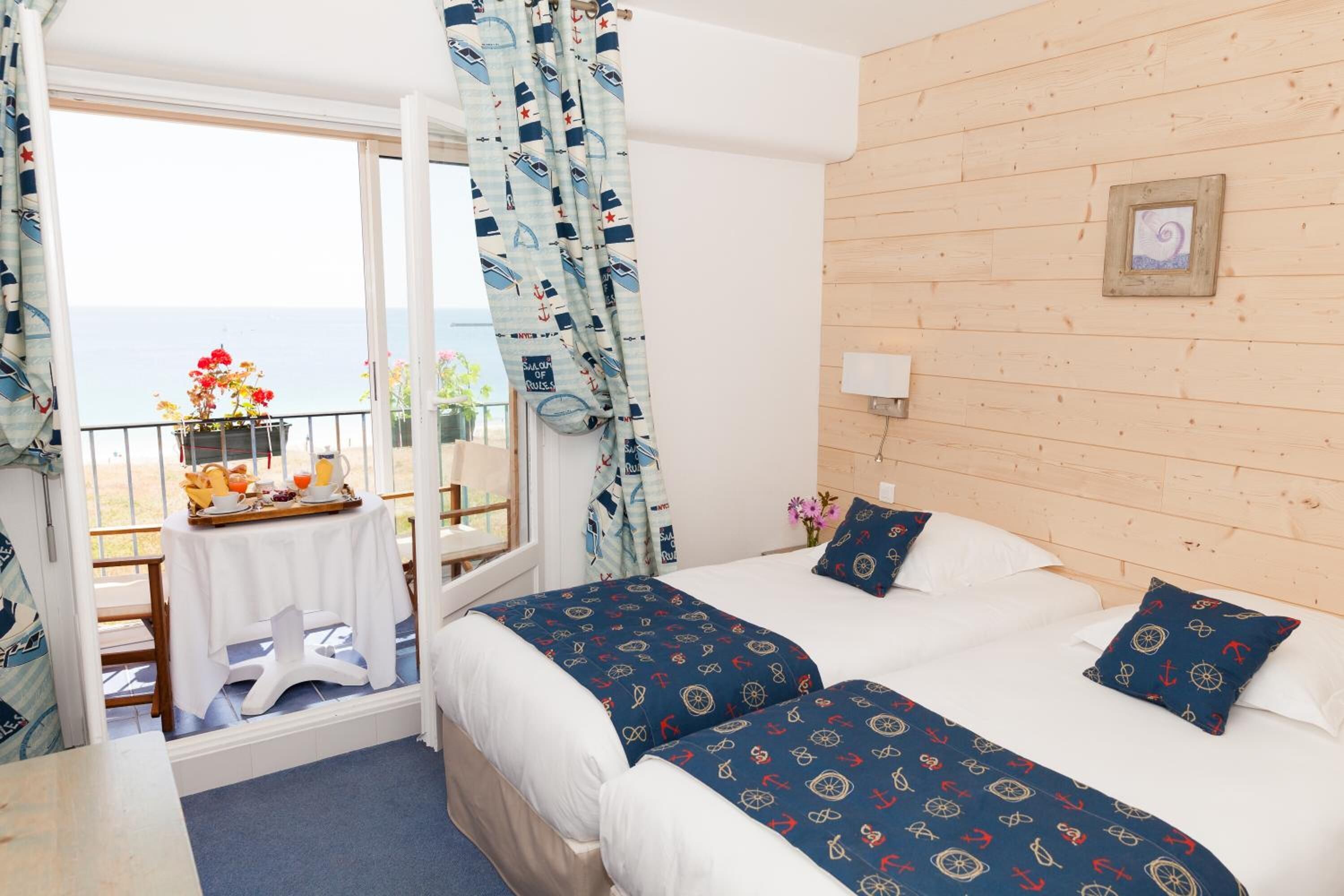 A hotel room with two beds, a balcony with a table and flowers, and a wooden wall.