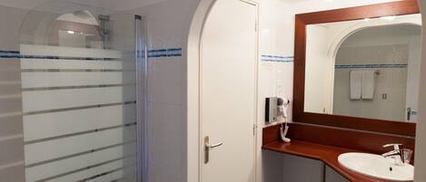 A bathroom with a glass shower enclosure, a white sink with a wooden countertop, and a mirror with a wooden frame.