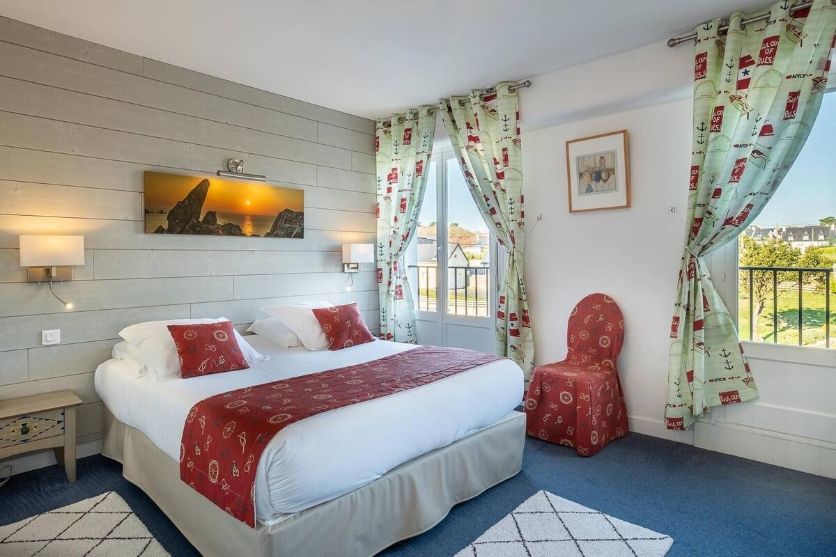 Ein Hotelzimmer mit einem großen Bett, einem Sessel, einem Gemälde und Blick ins Freie.