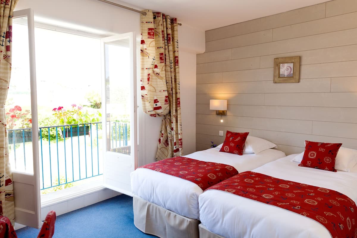 Ein Hotelzimmer mit zwei Betten, einem Fenster mit Vorhängen, einer Wandleuchte und einem Bilderrahmen.