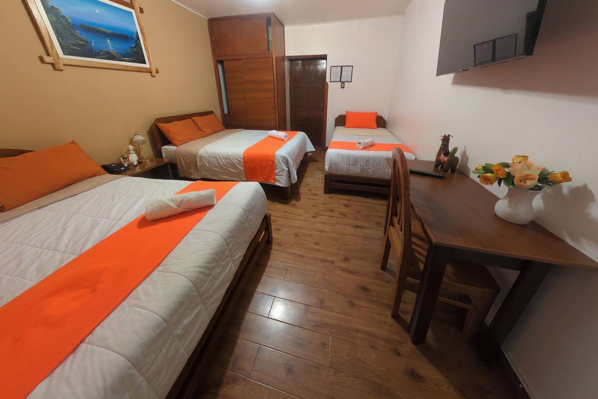 A hotel room with two beds, a desk, a chair, a TV, a painting, and a wooden floor.