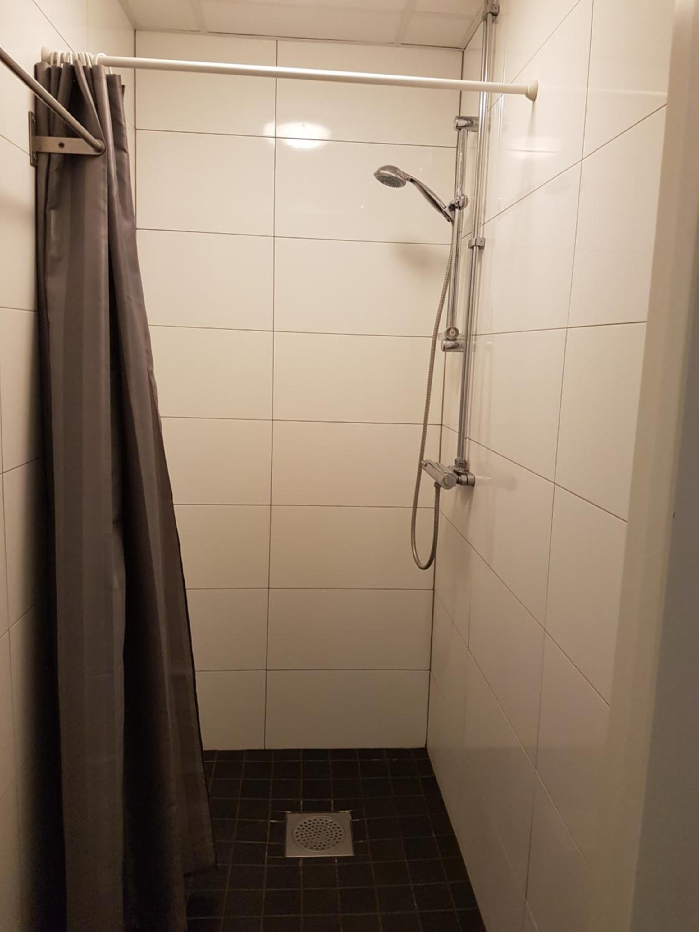 A small, tiled shower stall with a showerhead and a curtain rod.