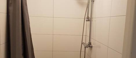A small, tiled shower stall with a showerhead and a curtain rod.